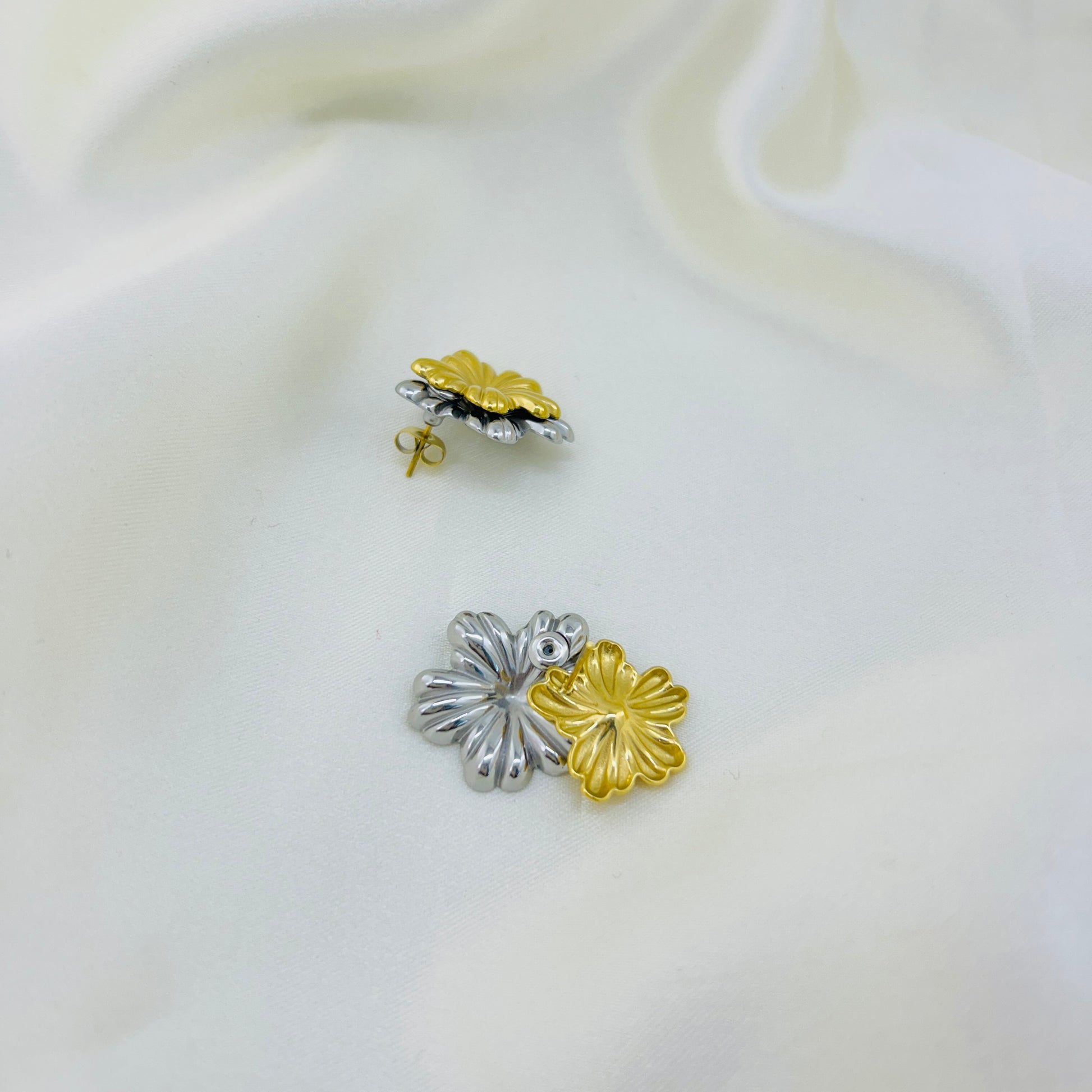 Pair of silver and gold flower-shaped earrings on a white background