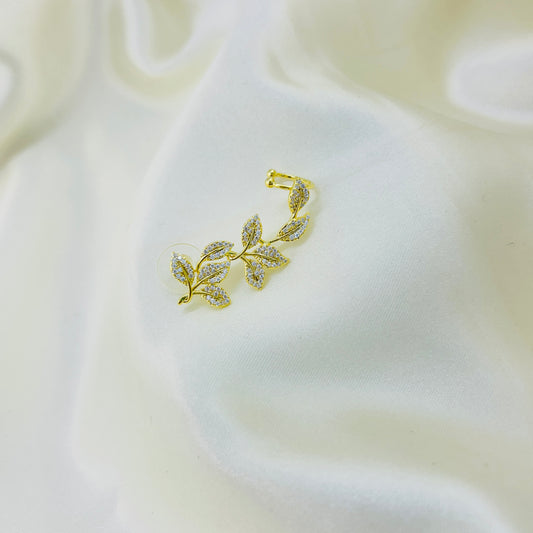 Gold leaf-shaped earring cuff on a soft white fabric background