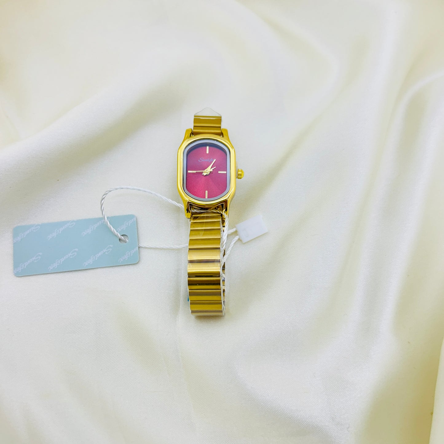 Gold watch with a pink face on a white fabric background