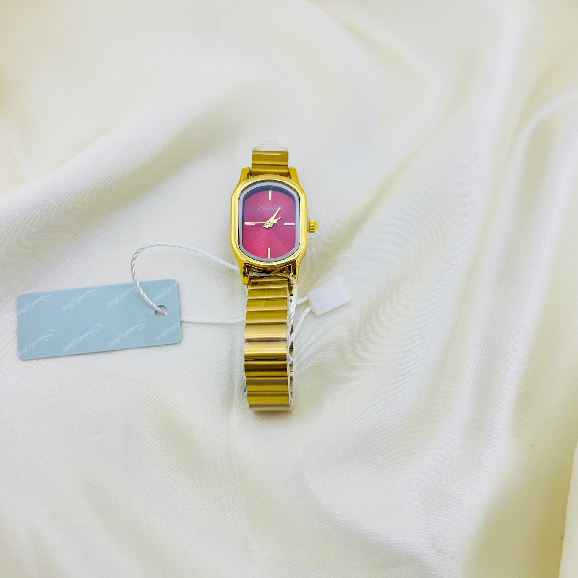 Gold watch with a pink face on a white fabric background