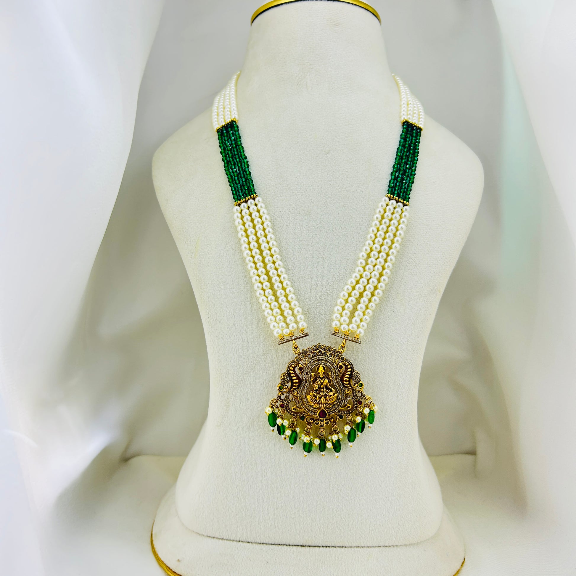 Pearl necklace with green beads and a gold pendant on a mannequin bust.