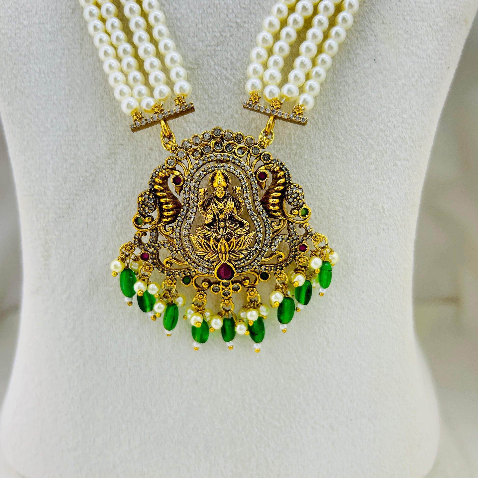 Gold necklace with green beads and a white pearl strand on a mannequin.