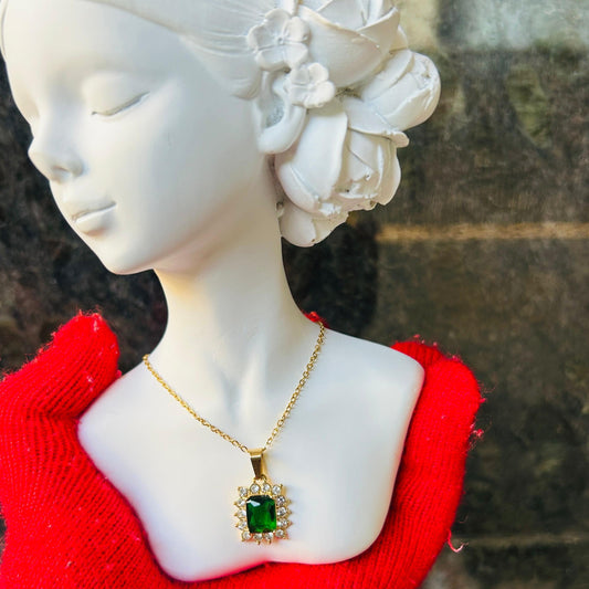 Mannequin head with white floral hairpiece and gold necklace with green pendant on red garment.