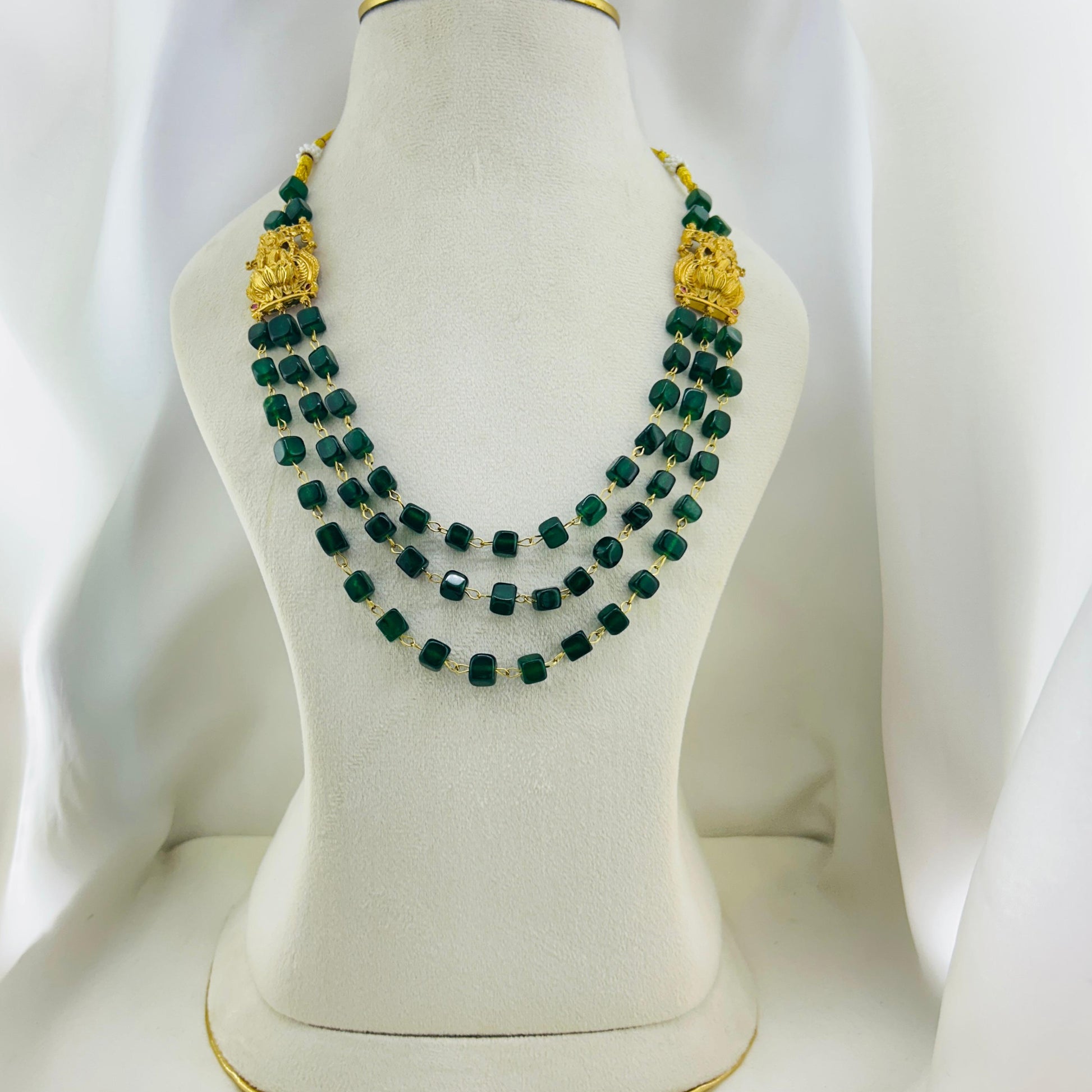Green beaded necklace with gold accents on a mannequin bust against a white background