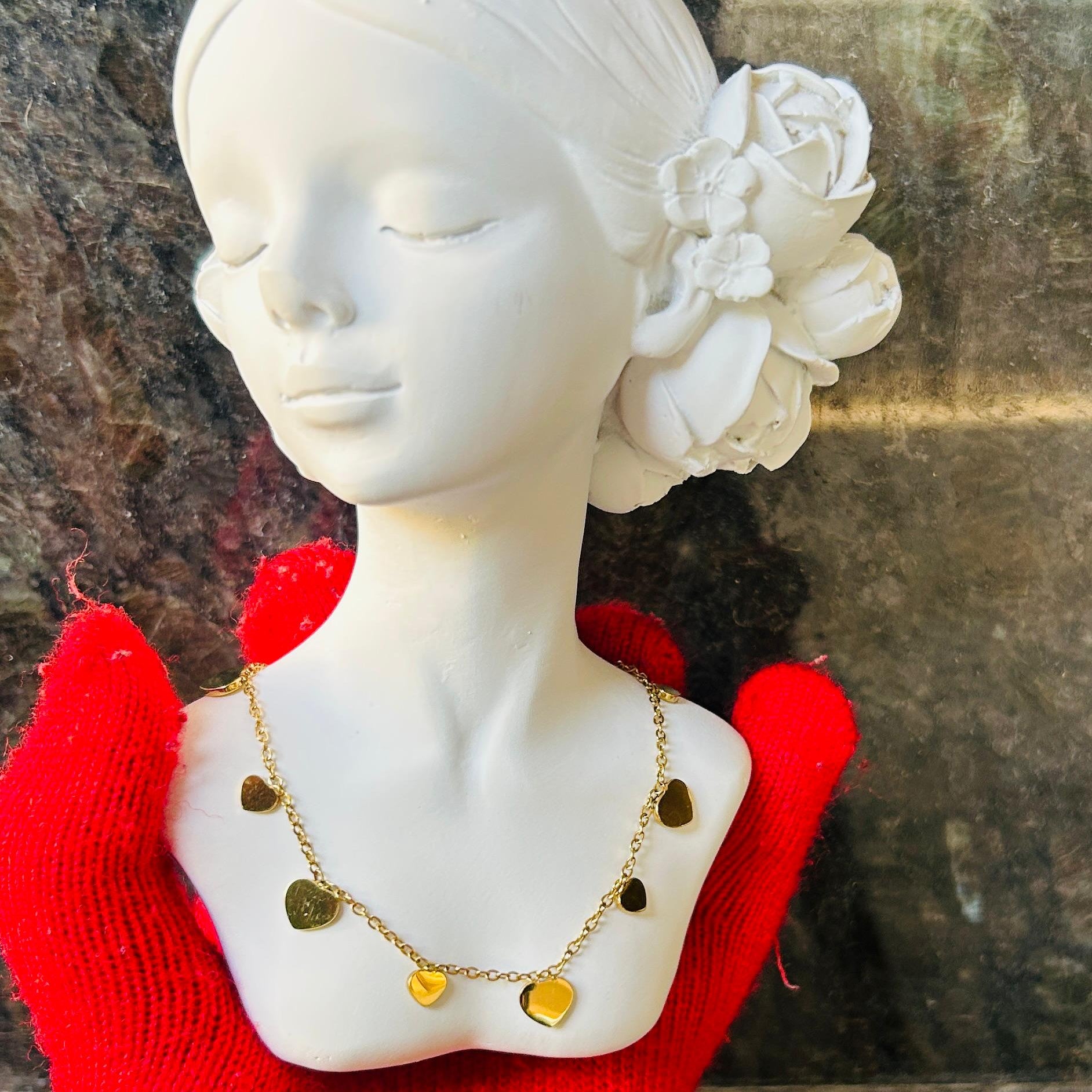 Mannequin head with white flowers in hair, red sweater, and gold necklace against a stone wall.