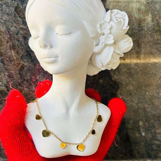 Mannequin head with white flowers in hair, red sweater, and gold necklace against a stone wall.