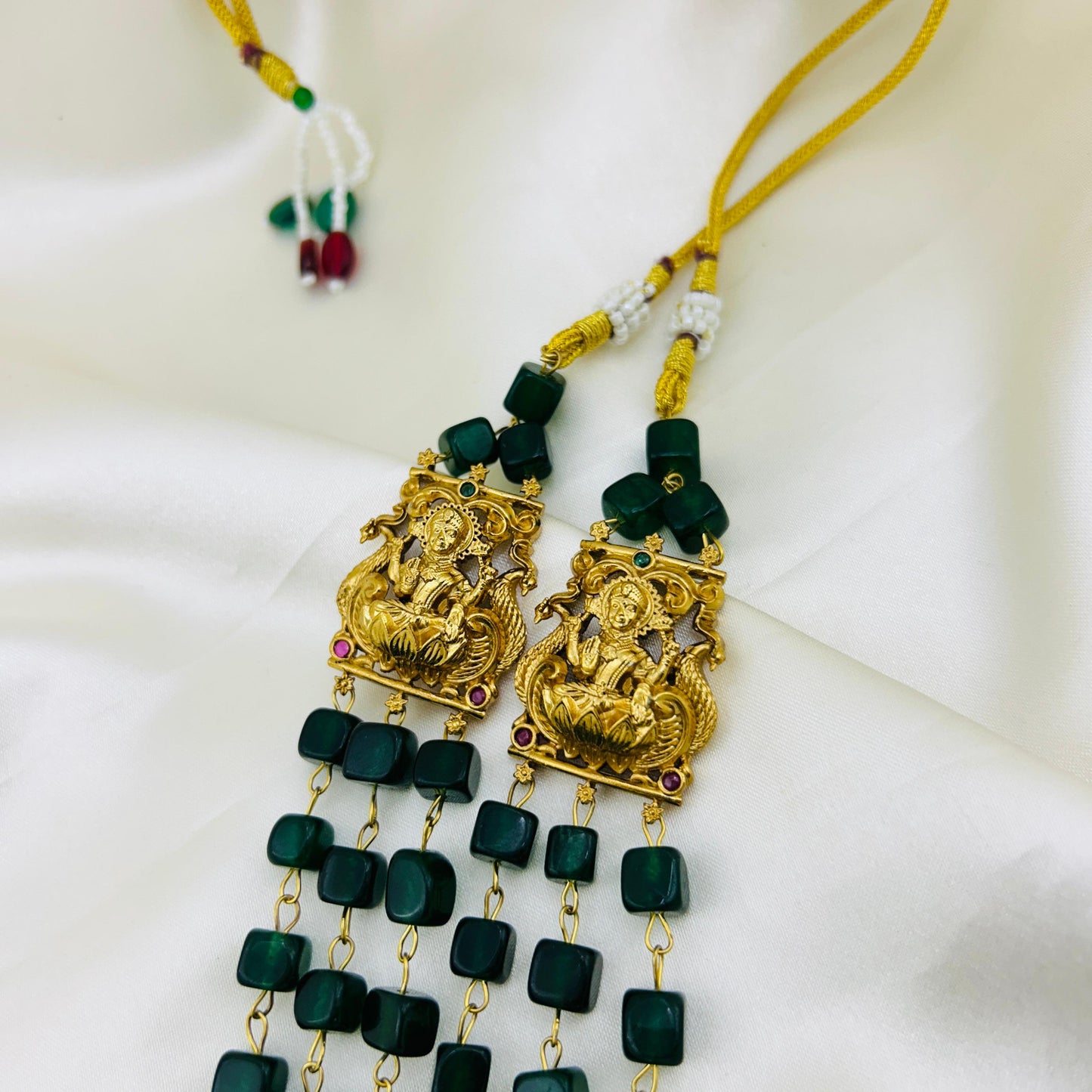 Gold and green jewelry piece on a white fabric background