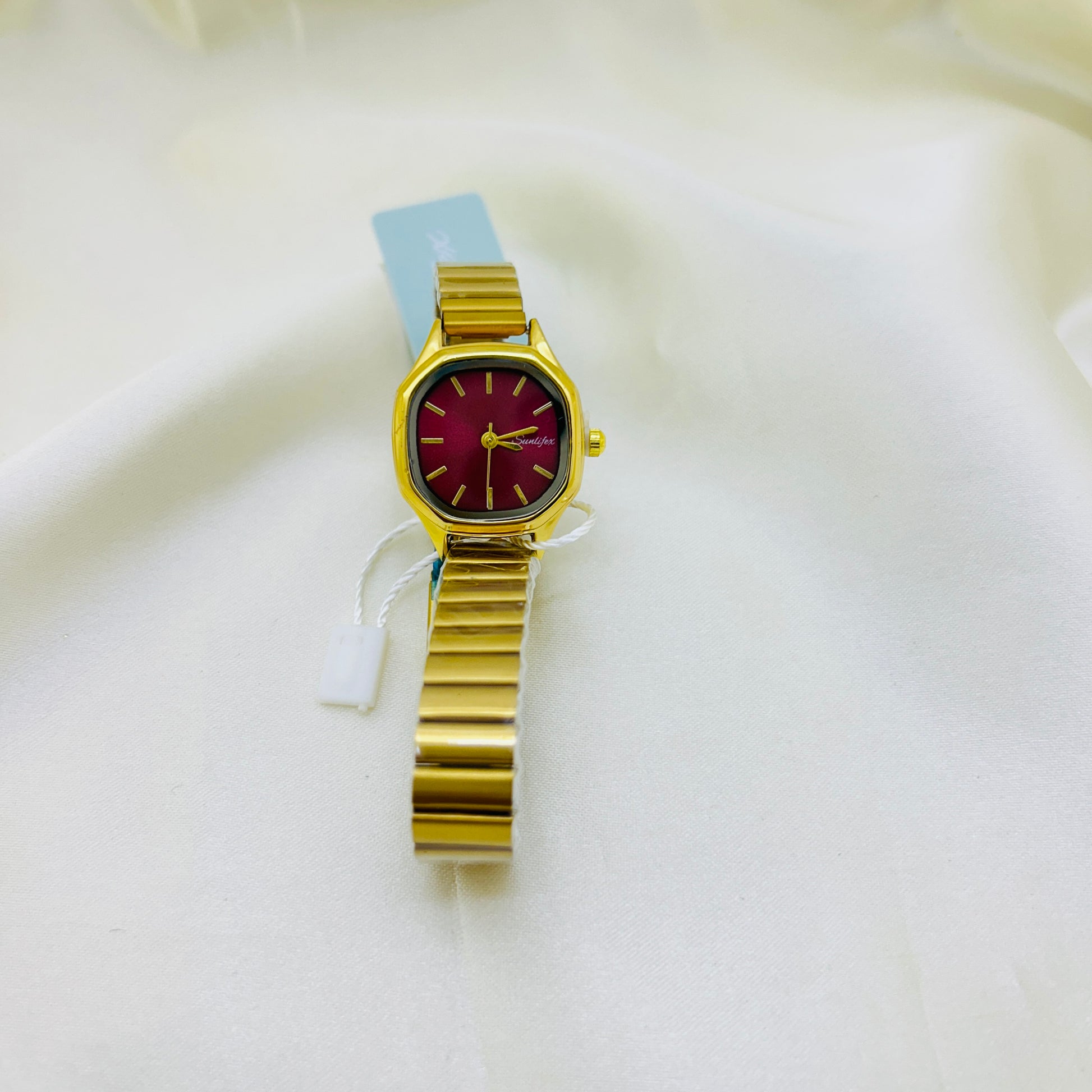 Gold watch with a magenta pink face on a white background
