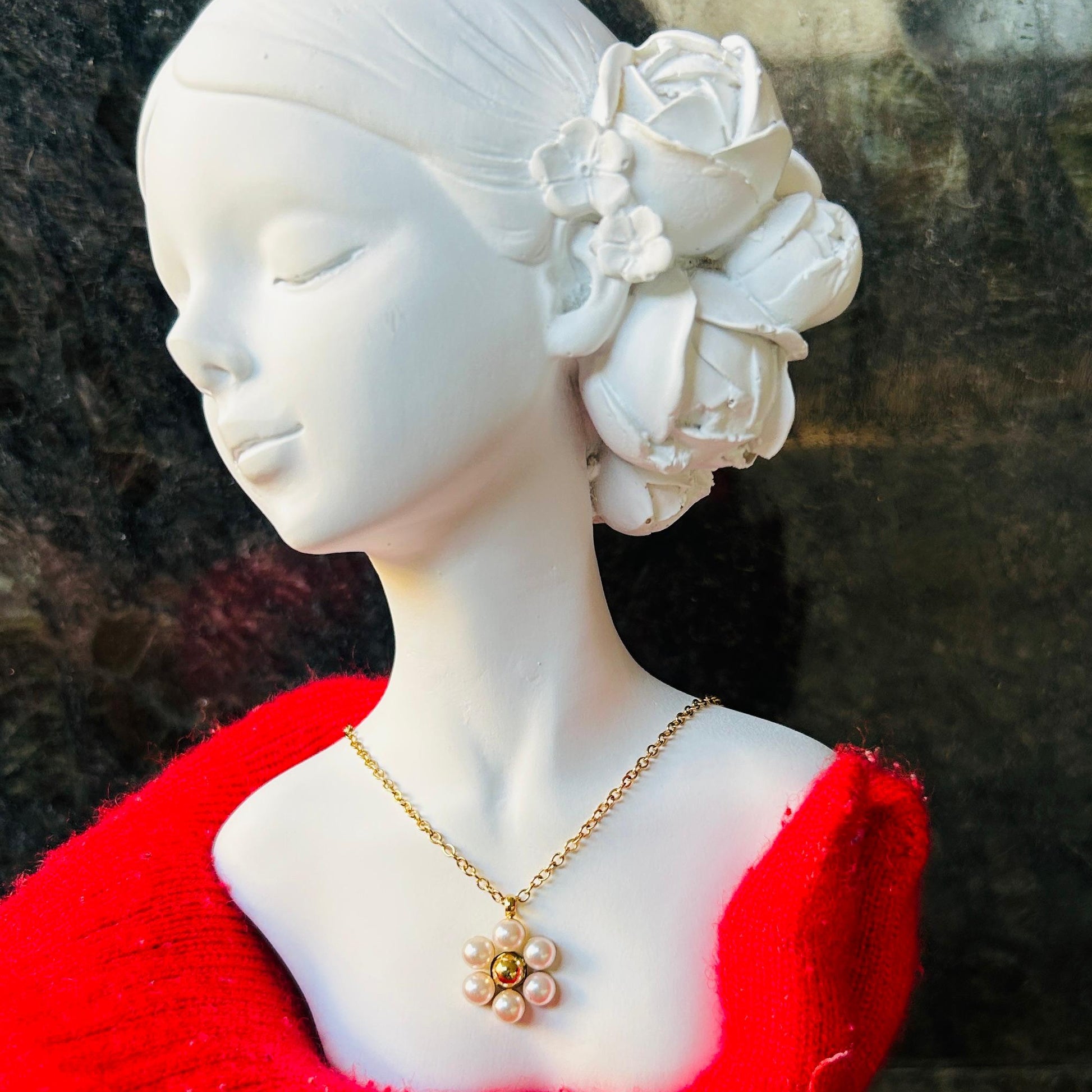 Mannequin head with red garment and gold pearl flower necklace against a dark background