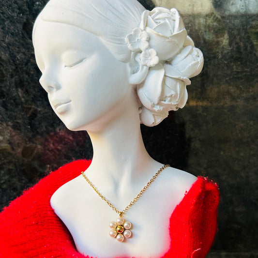 Mannequin head with red garment and gold pearl flower necklace against a dark background
