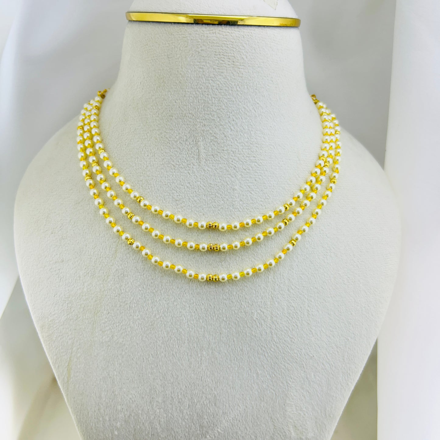 Three-layered swarovski pearl beaded necklace with yellow and gold beads on a mannequin bust.