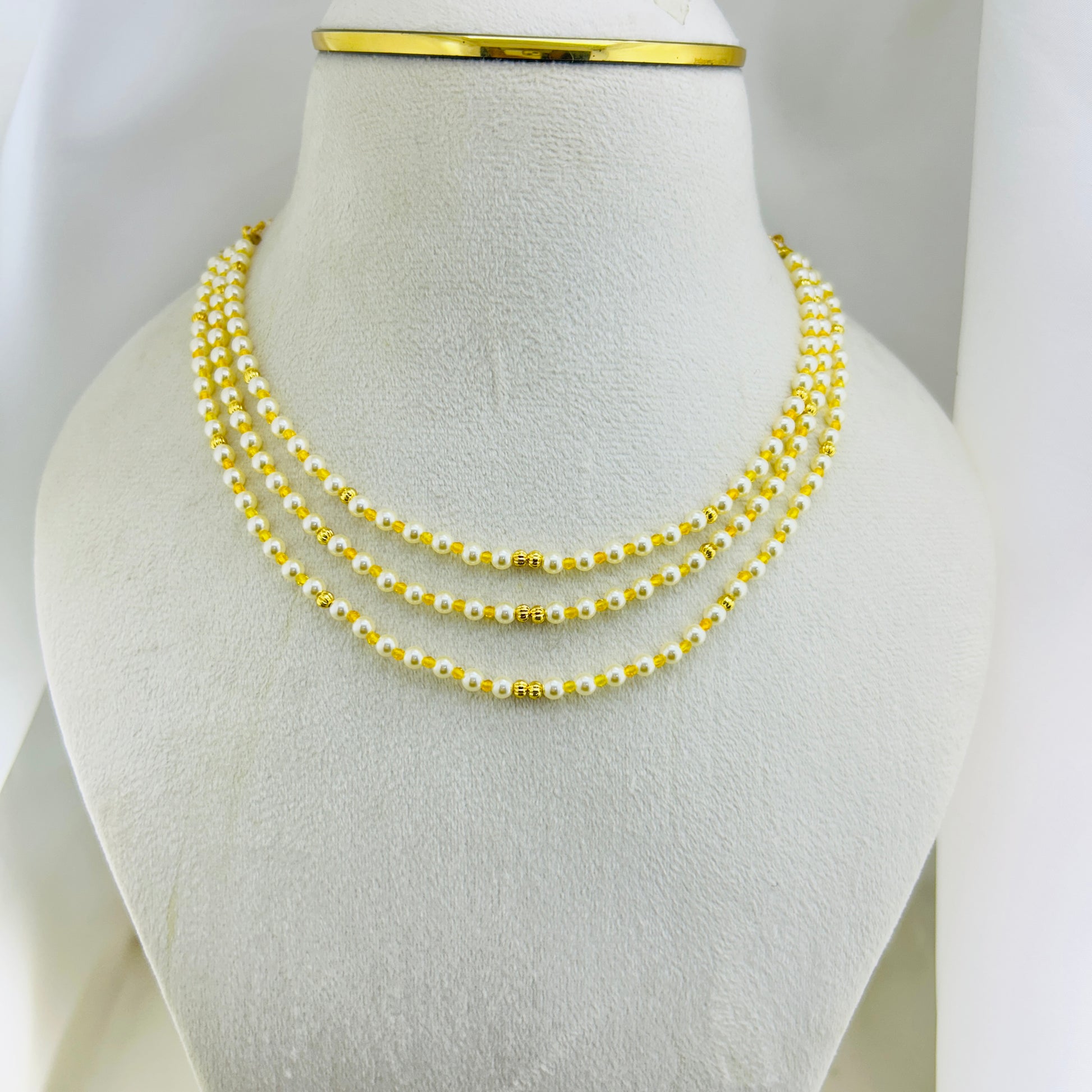 Three-layered swarovski pearl beaded necklace with yellow and gold beads on a mannequin bust.