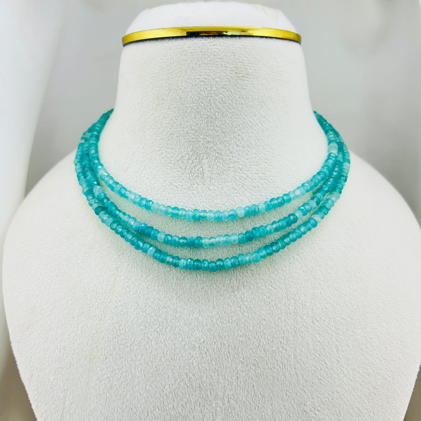Turquoise beaded necklace on a mannequin bust with a gold band.