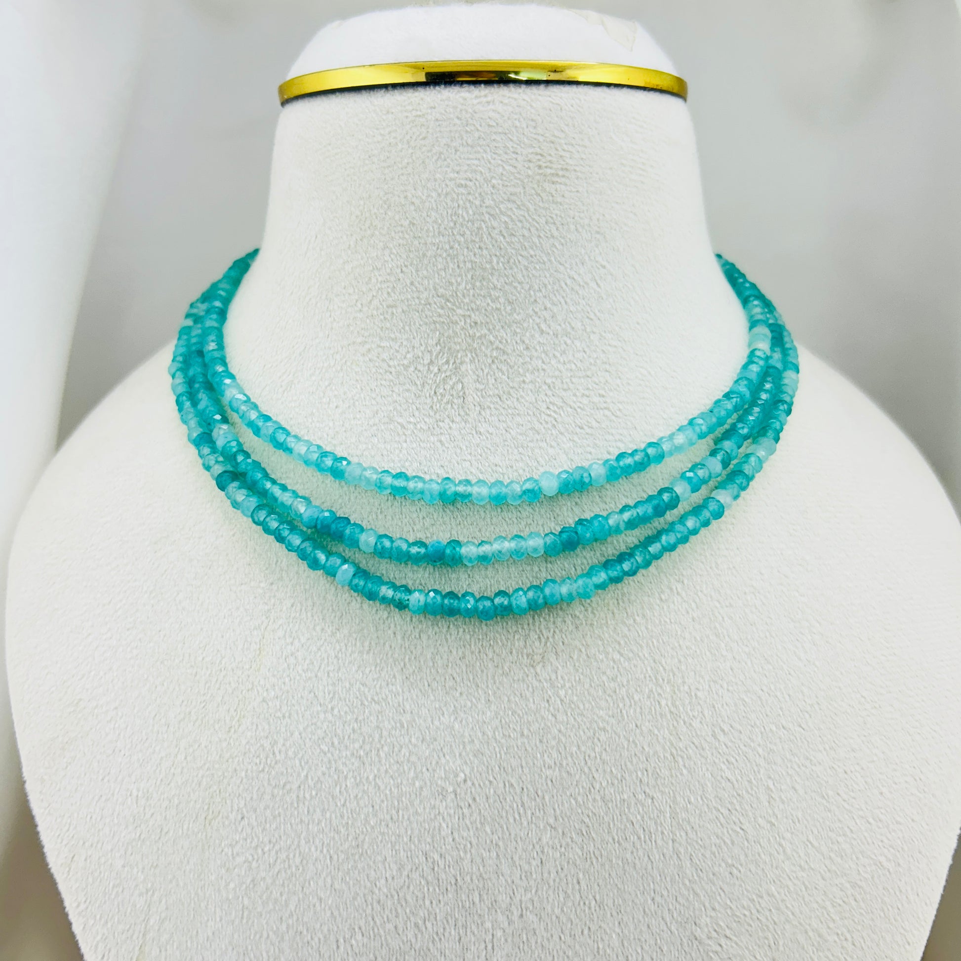 Turquoise beaded necklace on a mannequin bust with a gold band.